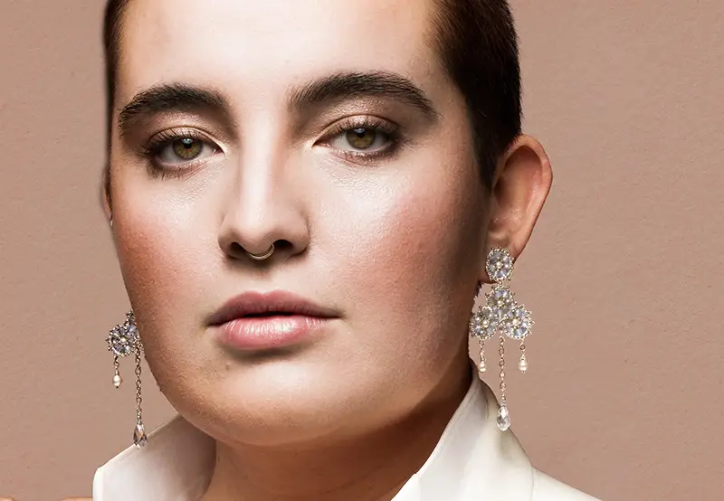 Beauty-Porträt, fotografiert von Ben Kunstleben in Freiburg. Eine Zusammenarbeit der Künstler Ben Kunstleben - Fotografie, Make-up von Nicolay Lissner, Zippora Zibold Schmuck und Christin-Marlen Freyler Styling. Das Bild zeigt das Model in elegantem Weiß, mit betonten Augen und glänzenden Ohrringen, die die subtile Eleganz und kunstvolle Ausführung des Teams hervorheben.